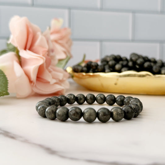 Pyrite beaded bracelet on a marble surface with pink flowers and a gold dish in the background.