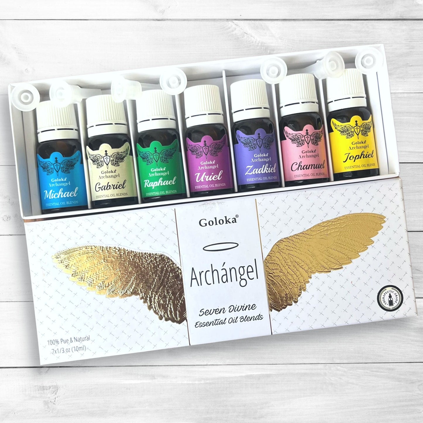 A set of seven therapeutic-grade essential oil bottles, each labeled with a different archangel's name and color (Michael - blue, Gabriel - green, Raphael - purple, Uriel - orange, Zadkiel - violet, Chamuel - pink, Jophiel - yellow). The box reads "**Archangel Essential Oil Blends**" with a gold wing design.