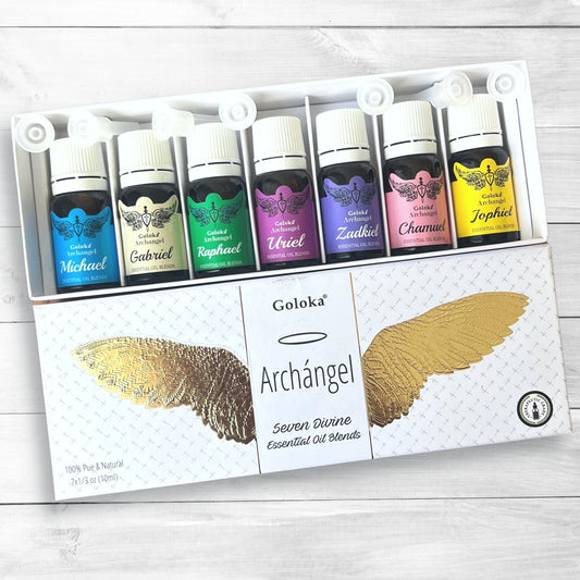 A set of seven therapeutic-grade essential oil bottles, each labeled with a different archangel's name and color (Michael - blue, Gabriel - green, Raphael - purple, Uriel - orange, Zadkiel - violet, Chamuel - pink, Jophiel - yellow). The box reads "**Archangel Essential Oil Blends**" with a gold wing design.