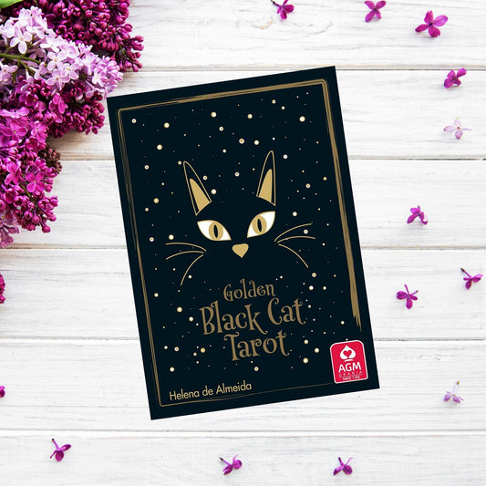A "Golden Black Cat Tarot" lies on a white wooden surface, surrounded by purple and magenta flowers. The cover features a stylized black cat with golden eyes and accents beneath a starry background. The author's name, Helena de Almeida, is displayed at the bottom.